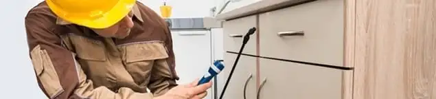 Roach exterminator applying treatment under kitchen cabinets in Chula Vista, CA