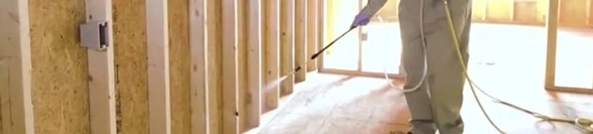 Termite treatment technician applying spray along framing and unfinished walls in Chula Vista, CA